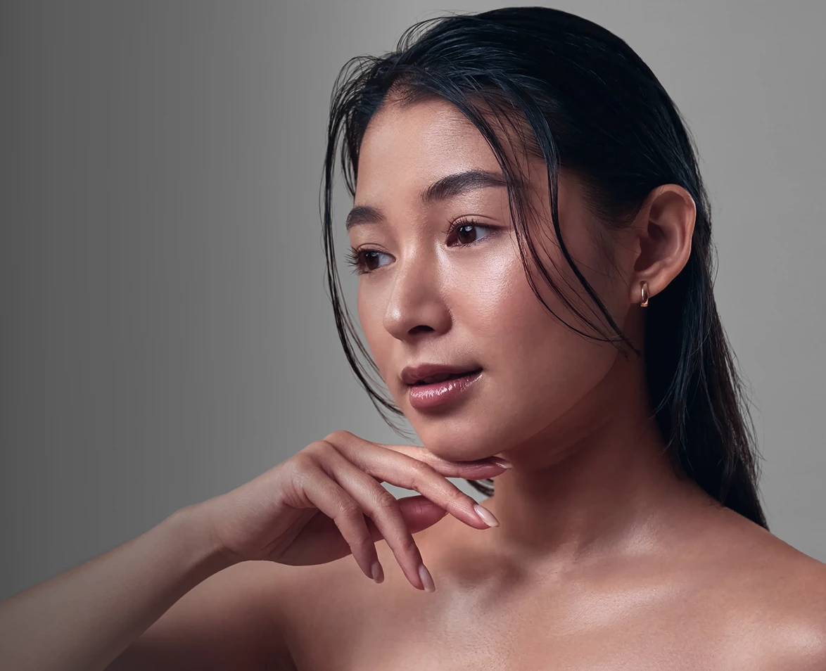Woman with clear skin touching her neck and shoulder against a neutral background